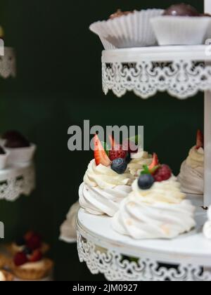 A vertical shot of meringues with raspberry, strawberry, and blueberry on a tray Stock Photo