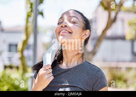 Feels good to fill my lungs with fresh air. a young woman taking off her face mask after going for a run outdoors. Stock Photo