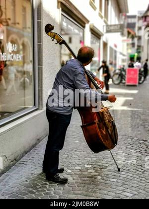 The vertical shot of an adult male man playing on  a double  bass on the street Stock Photo