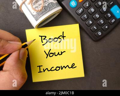 Hand holding pencil with the word Boost your income with banknotes and calculator on black background. Stock Photo