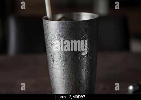 A closeup of a shiny metal cup with droplets of water on it against a blurred dark background Stock Photo
