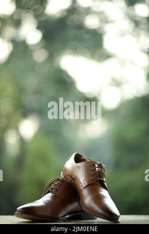 A selective focus shot of brown wedding shoes in front of trees Stock Photo