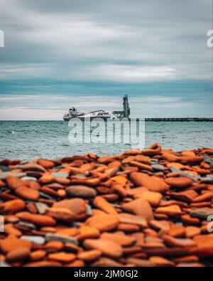 A vertical shot of pebbles on a beach with a ship in the background Stock Photo