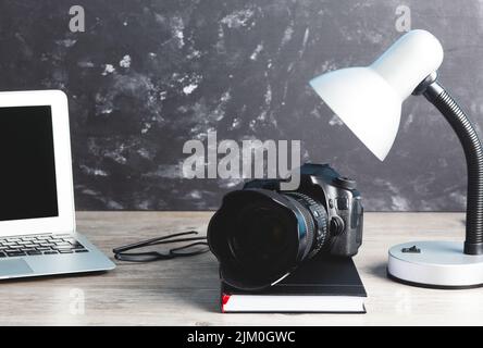 The photographer workstation with a camera, laptop, glasses on the wooden table Stock Photo