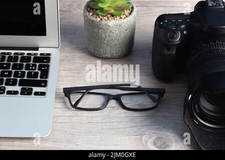 The photographer workstation with a camera, laptop, glasses on the wooden table Stock Photo