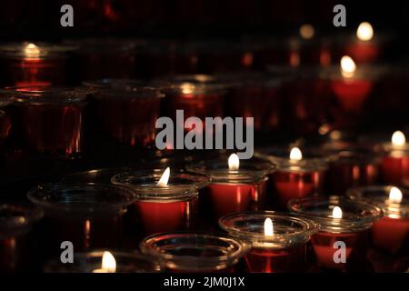A selective focus shot of row lines of lighted candles arranged in a dark room Stock Photo