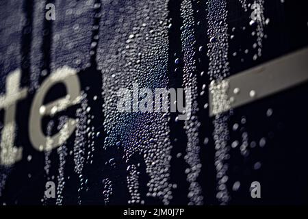 A closeup of small water drops on a surface of black glass with letters visible from left Stock Photo
