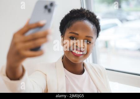 African woman starting a live video clip from her modern mobile phone. Shadow from window. Taking selfie Stock Photo
