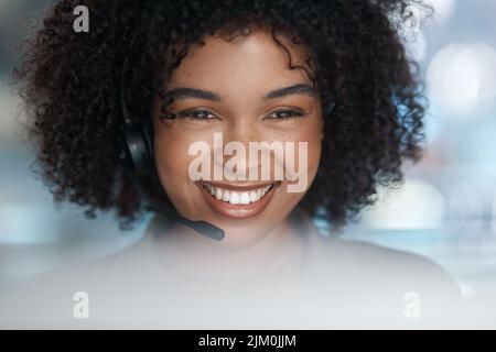 Webcam on. a young female agent smiling over her monitor with her headset on while working in a call centre. Stock Photo