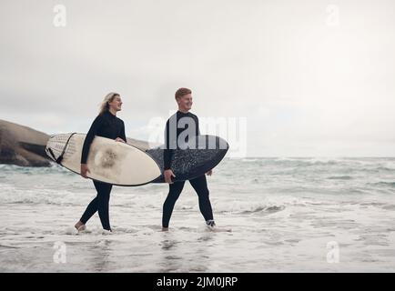 To become a good surfer, you need to understand the ocean. a young couple out at the beach with their surfboards. Stock Photo