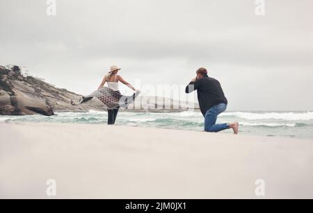 Pictures are better with a good view. a man taking pictures of his girlfriend while spending time at the beach. Stock Photo
