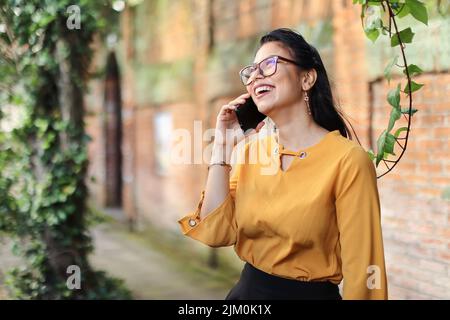 Young brunette Latin American woman talking on the phone wearing eyeglasses smiling Stock Photo