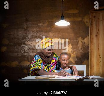 A Rwandan mother helping her child with homework at home with a light shining on them Stock Photo