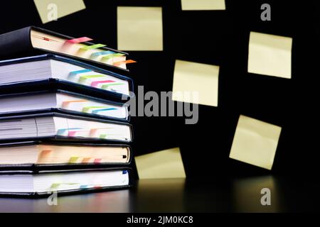 Close-up of a stack of office notepads with colorful sticky page markers sandwiched between pages on dark background with yellow paper sticker notes Stock Photo