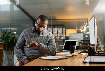 Nows a good time to call it a night. a handsome mature businessman sitting at his office desk and checking his watch during a late shift. Stock Photo