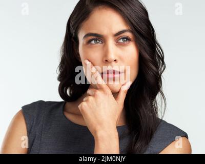 Whats on your mind. a beautiful young woman looking thoughtful while standing against a white background. Stock Photo