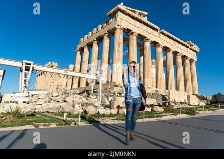 A vertical shot of a Caucasian blonde woman posing in front of Acropolis, Athens Stock Photo