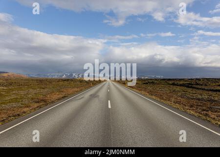 A scenic view of an empty asphalt road surrounded by dried fields on a cloudy day in Iceland Stock Photo