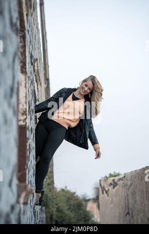A vertical shot of a Caucasian woman hanging from a wall, smiling Stock Photo