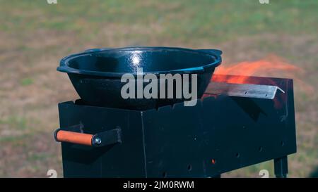 A closeup of a grill with fire coming out of it with an empty pot on it surrounded by lush grass Stock Photo