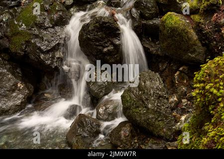 Closeup of a waterfall, water cascading over large boulders surrounded by moss covered rocks. Stock Photo