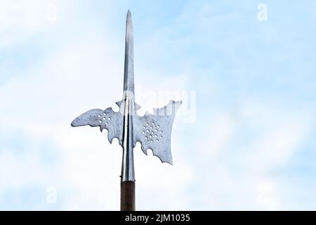 Metal top of a halberd, also called halbard, halbert or Swiss voulge, with axe blade and spike against a cloudy blue sky, pole weapon, copy space, sel Stock Photo