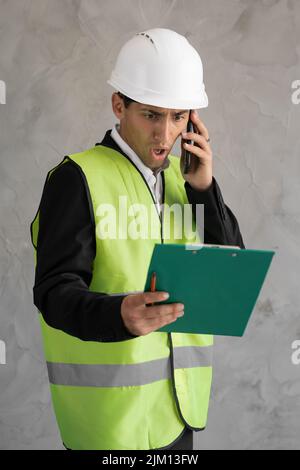 Angry Arabic architect screaming at phone during call making angry gesture with hand isolated on grey studio background. Despair engineer with Stock Photo