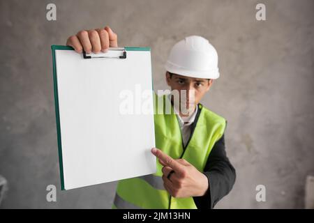 Angry arabic man engineer or architect wearing a hard hat pointing at empty clipboard Stock Photo