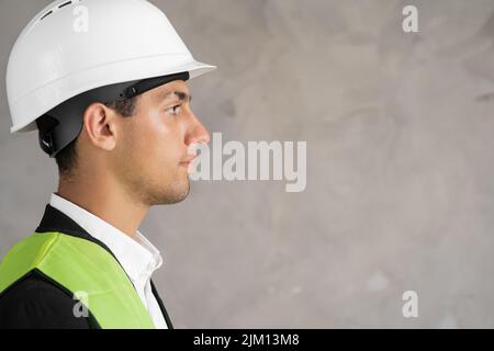 Studio profile portrait of young arabic man architect, builder engineer, wearing white construction safety helmet isolated on grey background. Stock Photo