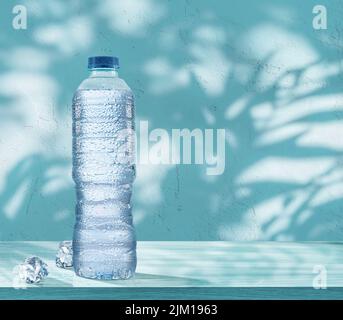 Plastic bottle of chilled water with condensation drops and two ice cubes on the table. Blue background. Stock Photo