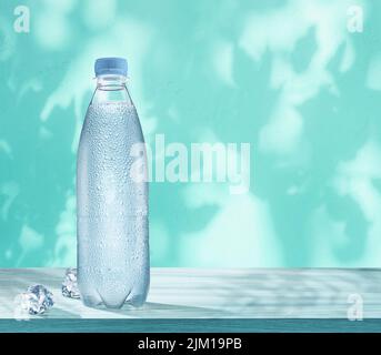 Plastic bottle of chilled water with condensation drops and two ice cubes on the table. Wall with leaf shadows at the background. Stock Photo