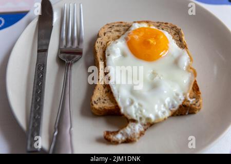 A fried egg on a slice of toasted bread on a plate with knife and fork. Stock Photo