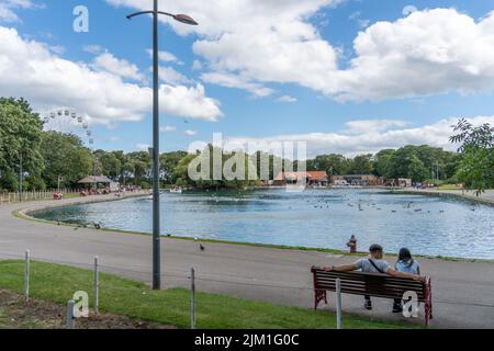 View of the lake at South Marine Park, South Shields, UK with a young couple sitting on a bench. Stock Photo