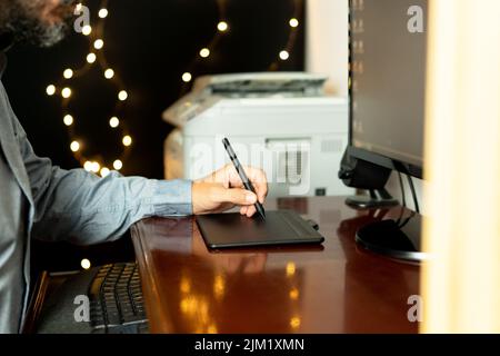 Young left-handed graphic designer sitting at his workspace using digital graphic tablet. Working professional. Freelance. Stock Photo