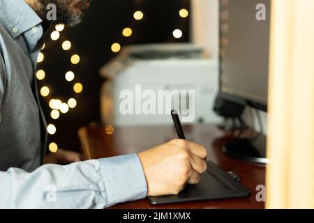Young graphic designer sitting at his workspace using digital graphics tablet. Working professional. Freelance. Stock Photo