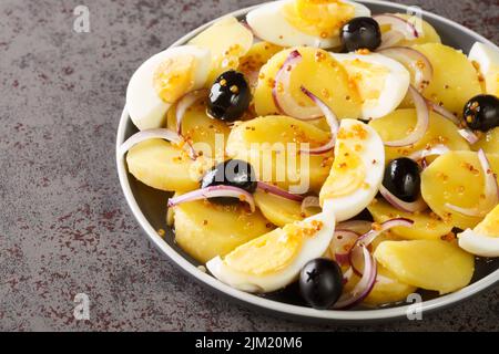 Potato salad with boiled eggs, onions and olives seasoned with mustard sauce close-up in a plate on the table. horizontal Stock Photo