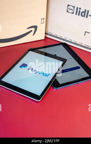 Berlin, Germany - August 4, 2022: Two mobile tablets with the home screen of an international payment service provider in front of shipping boxes. Stock Photo