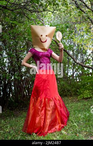 A young woman without a face looks in the mirror. Wearing a paper bag with a smiling face drawn on it. The woman feels happy. Stock Photo