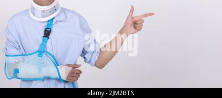 Portrait of smiling Asian man with broken arm and neck pointing finger to empty space isolated on white background copy space for text Stock Photo
