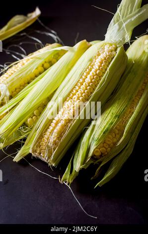 Fresh young sweet corn on cobs on rustic dark table close up, harvest concept Stock Photo