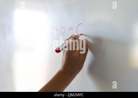 Cropped hand of caucasian female teacher writing formula on whiteboard during math class Stock Photo