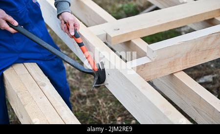 Man worker building wooden frame house on pile foundation. Carpenter removing nail from wooden joist, using hammer. Carpentry concept. Stock Photo