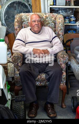 Senior man sitting in old armchair in his shed Stock Photo