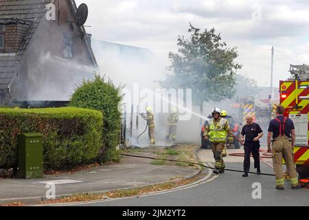 Fire Engines & firemen from Essex Fire & Rescue Service just arrived at house fire burning between timber boundary fence & residential property UK Stock Photo