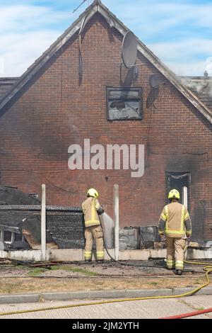 Firefighters damping down house fire after firemen dealt with flames in Alamy 2JM2YYJ damage to UPVC facias door window frames dormer Essex England UK Stock Photo