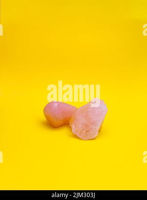 Polished rose quartz and rough/raw rose quartz crystals on a plain, bright yellow background with copy space. Stock Photo