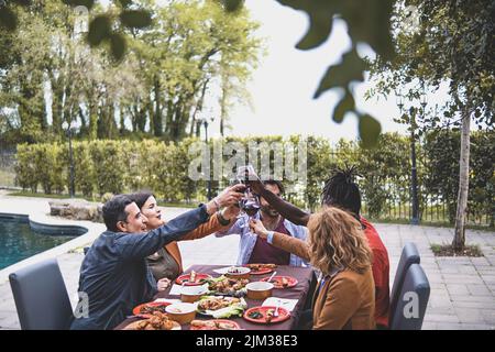 Multiracial group of friends having a celebratory toast during the birthday dining in the courtyard of the farmhouse by the pool - people lifestyle an Stock Photo