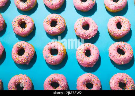Full frame shot of fresh pink donuts with sprinklers arranged on blue background Stock Photo