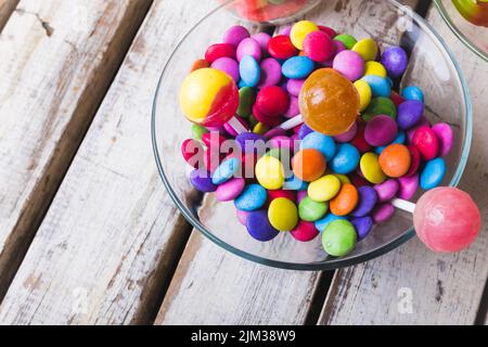High angle view of multi colored lollipops and chocolate candies in glass bowl on wooden white table Stock Photo
