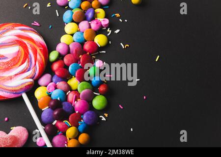Overhead view of lollipop with colorful candies and sprinklers by copy space on black background Stock Photo